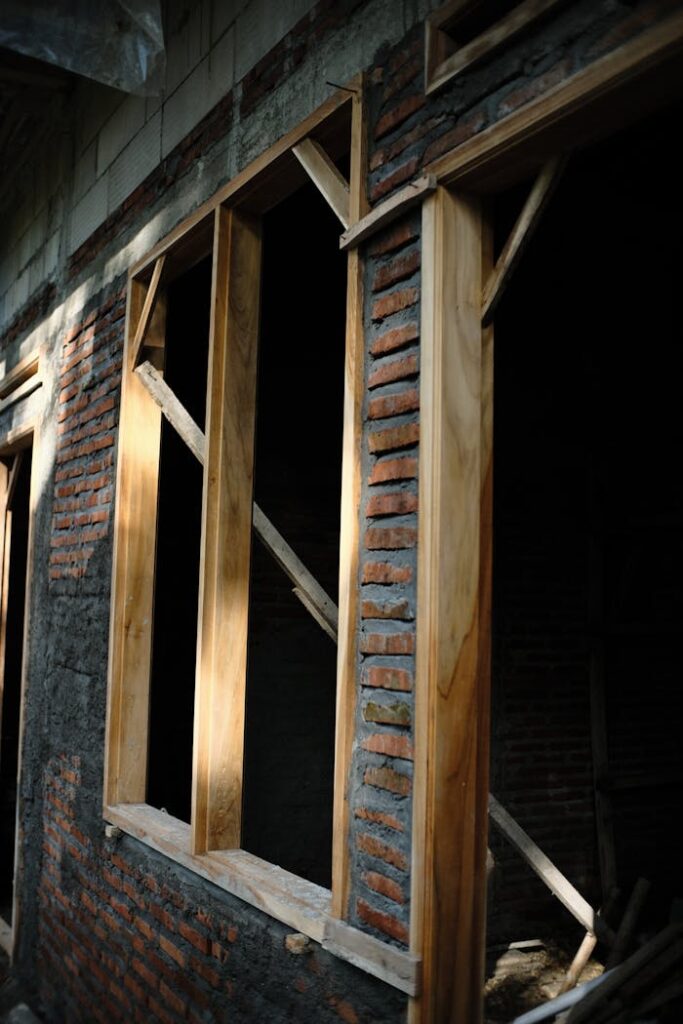 An unfinished building exterior featuring wooden window frames set in a brick wall.